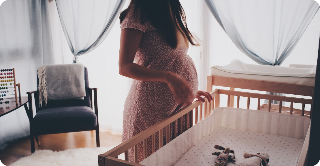 Pregnant woman standing in front of baby bed
